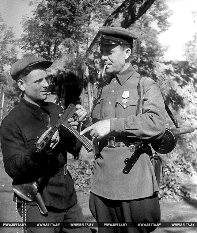 Партизанский оружейник - Яков Менкин (слева) передает сделанный им автомат командиру отряда имени Котовского Николаю Баранову. 1943 год